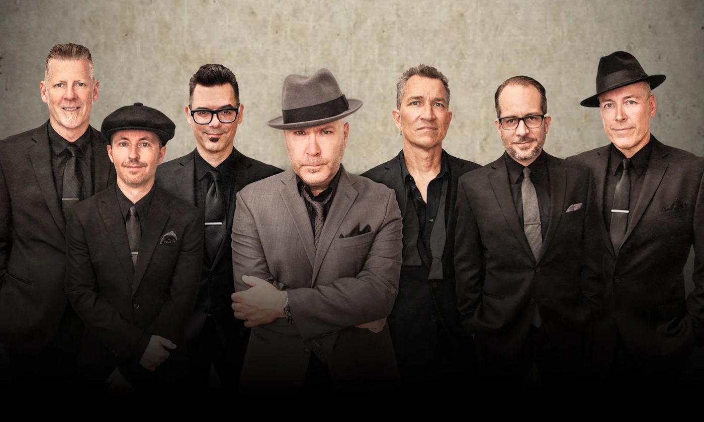 Bandmates from Big Bad Voodoo Daddy pose in front of a gray backdrop.
